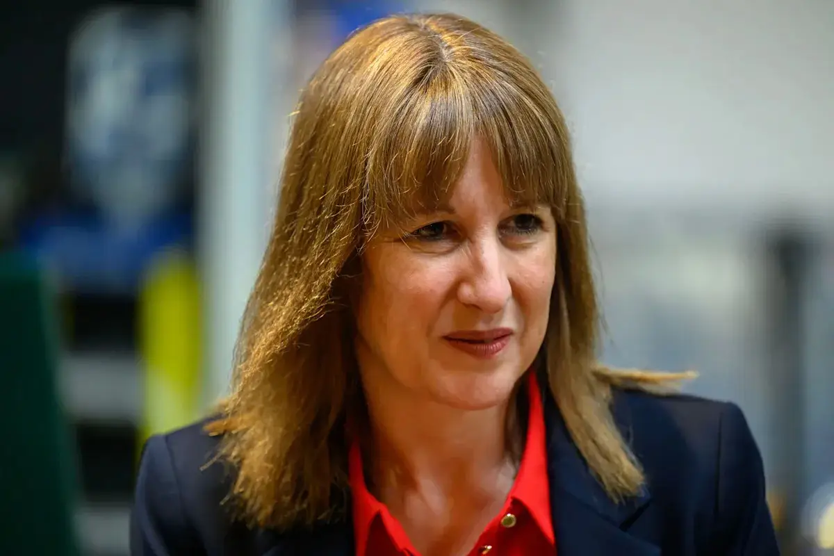 Woman with shoulder-length brown hair wearing a dark blazer and red shirt, looking to the side indoors
