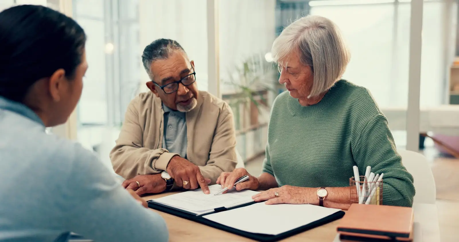 Three people reviewing documents together at a table in a bright office setting