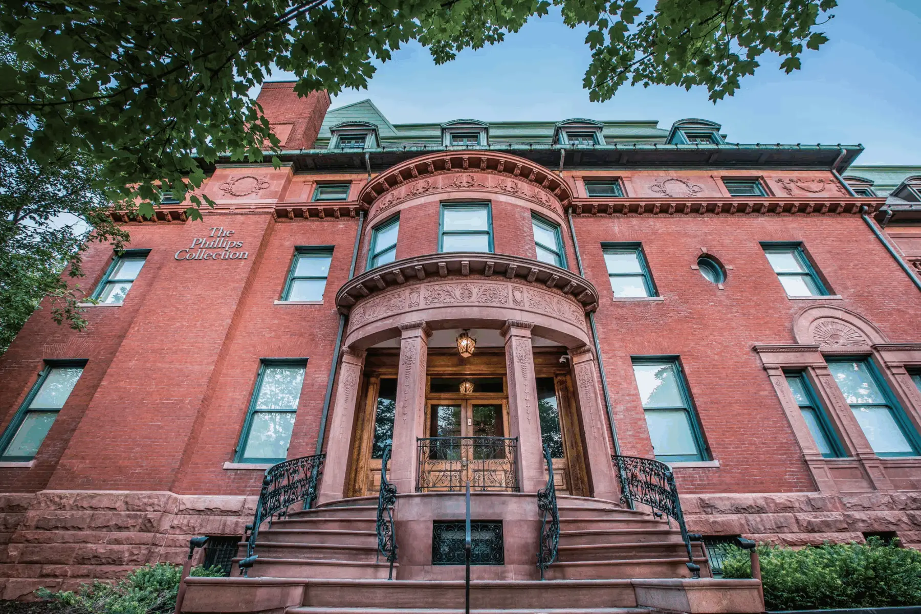 Red brick mansion with curved portico, ornate stone details, and dormer windows, labeled "The Phillips Collection