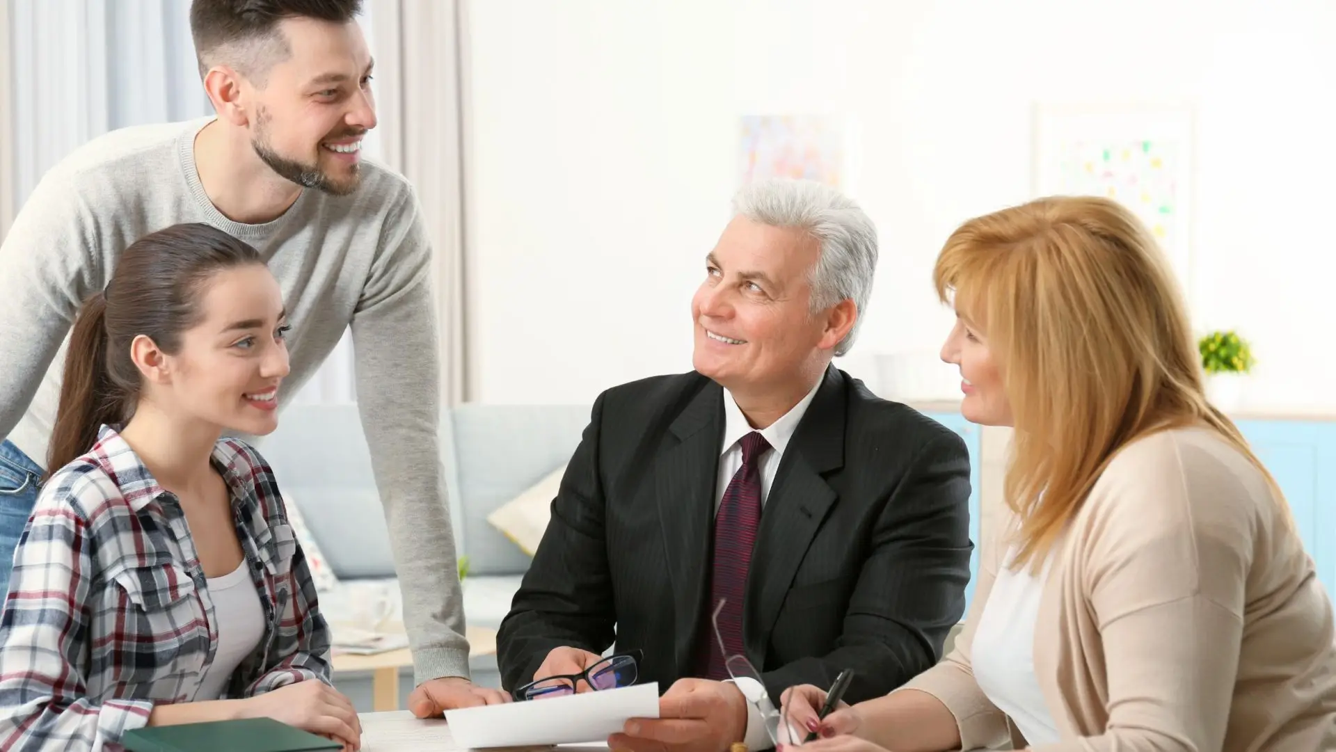 A financial advisor in a black suit meets with a family of four around a table with documents
