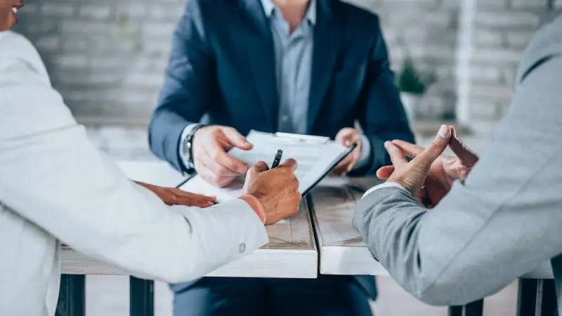 Three business professionals review documents together at a table during a meeting