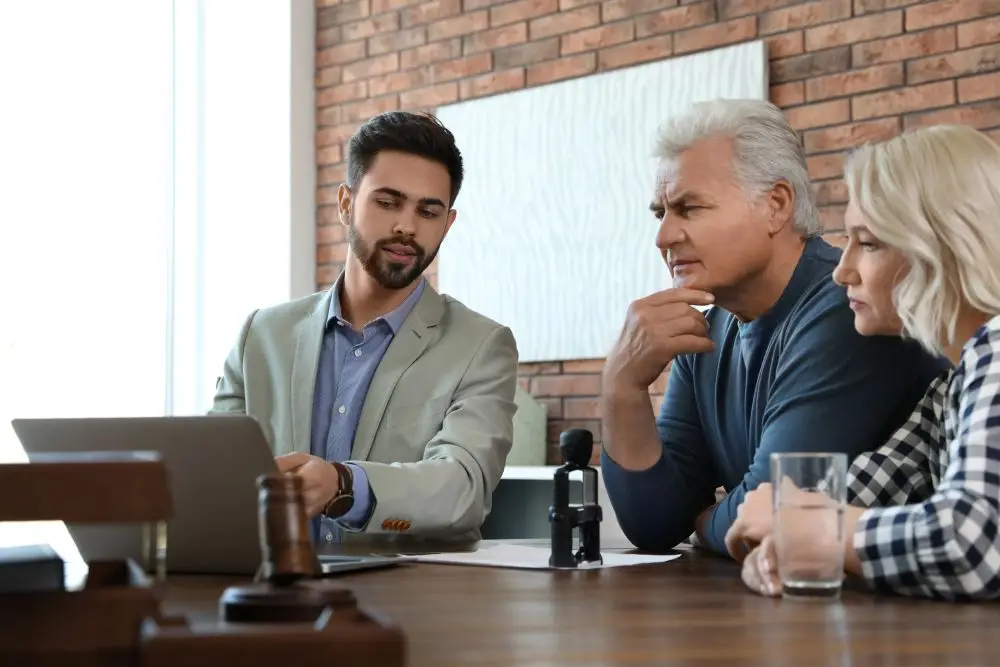 Four people sit at a table with a laptop and microphone during a professional meeting in a brick-walled office