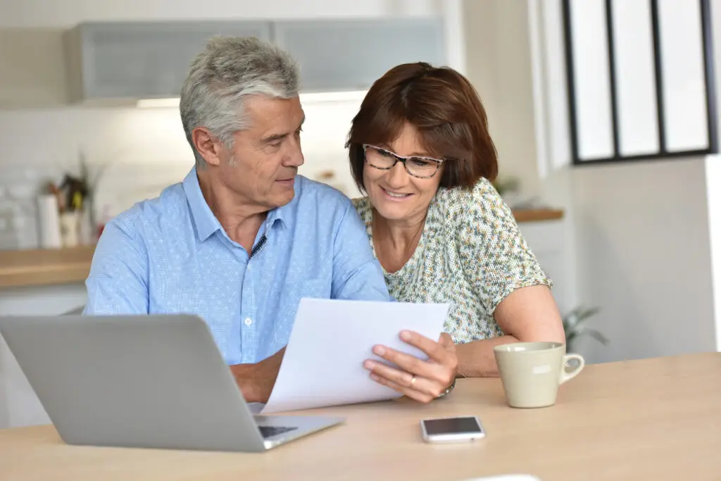 Mature man and woman at table with laptop, tablet, and coffee cup reviewing documents together