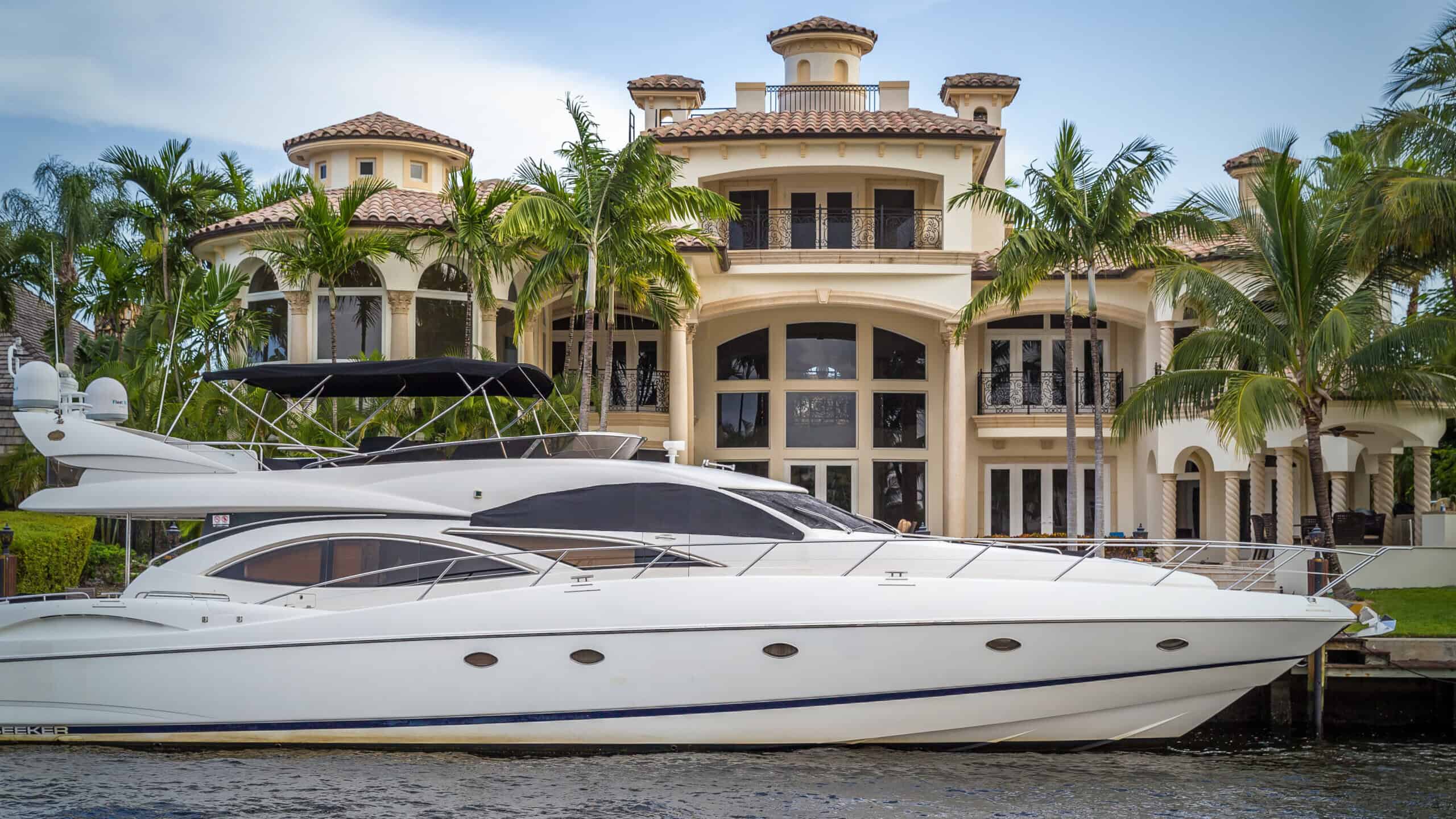 Luxury waterfront mansion with palm trees and a docked white motor yacht