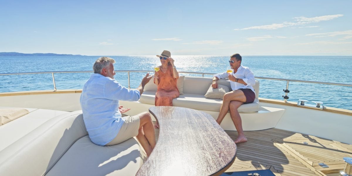 Four people on a luxury yacht deck socializing with drinks and ocean view in background