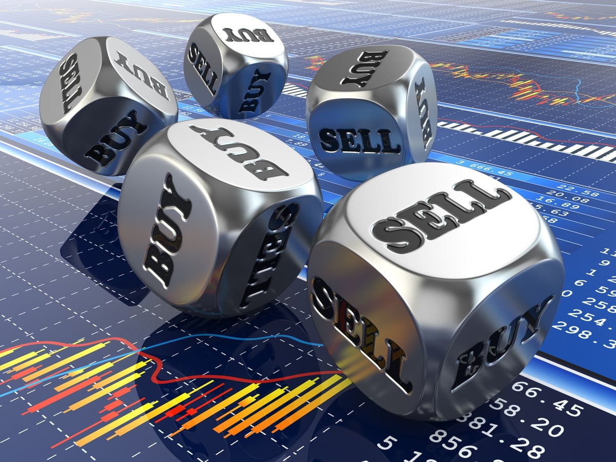 Metallic dice displaying financial terms like "BUY," "SELL," and "HOLD" on a blue stock market data background