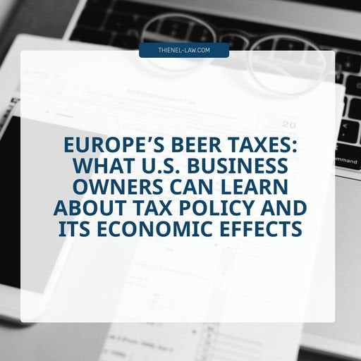 Document and glasses on laptop keyboard with blue banner text about European beer taxes and US business tax policy