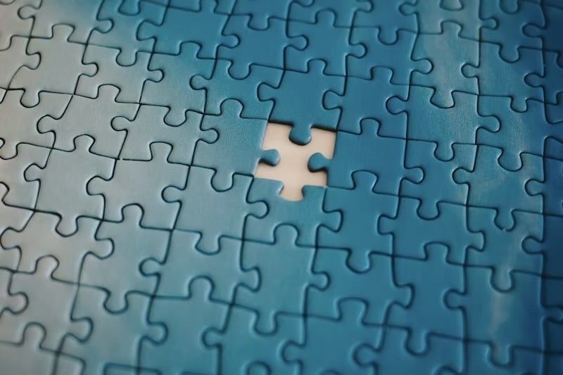 One blank puzzle piece missing from a completed blue jigsaw puzzle, revealing white space beneath