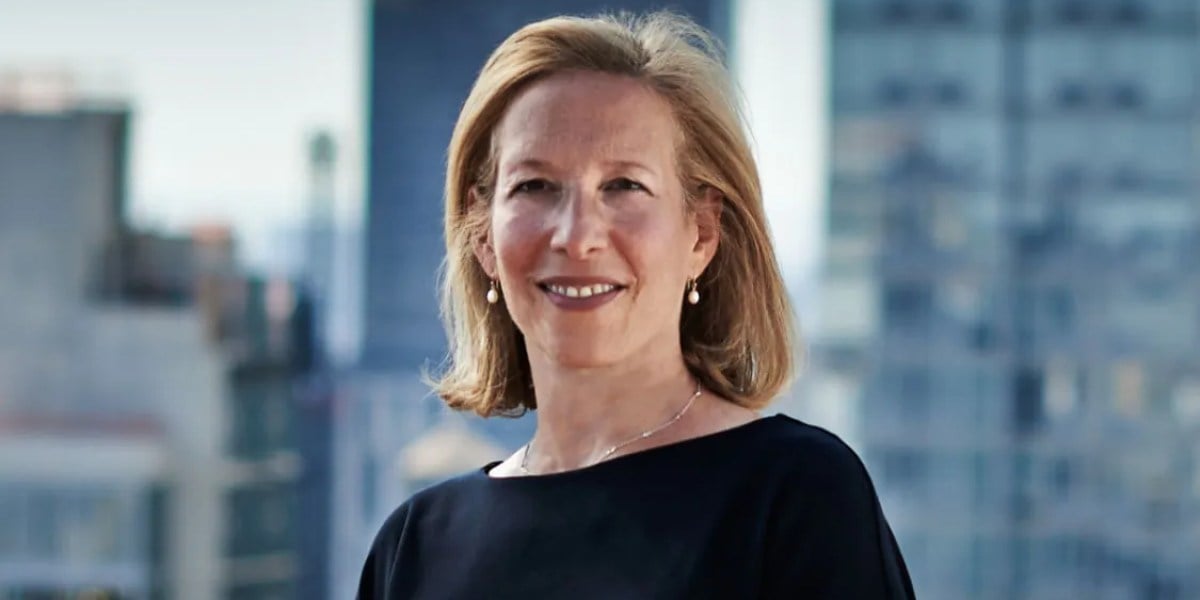 Professional headshot of a woman with shoulder-length reddish-brown hair wearing a black top against a blurred city skyline background