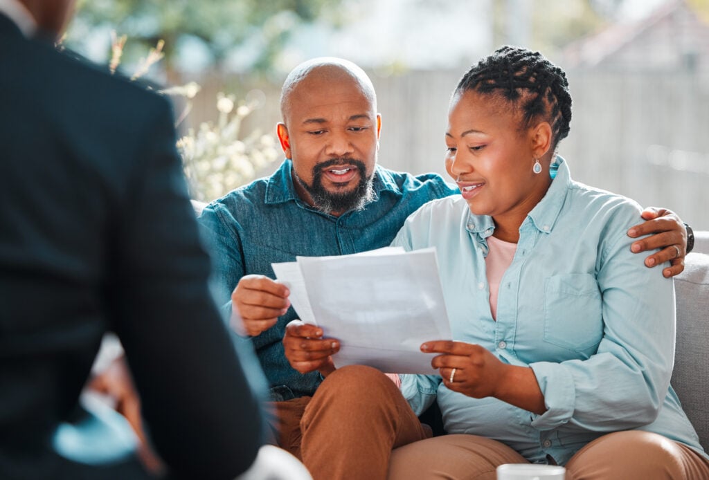 A man and woman sit together reviewing a document while speaking with a professional in business attire