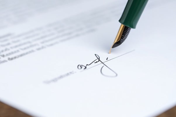 Green fountain pen signing a document with printed text visible in the background